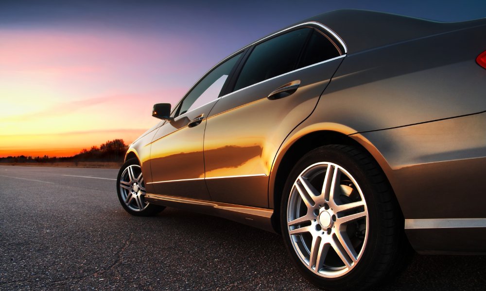 gray luxury car on an asphalt road looking at a setting sun
